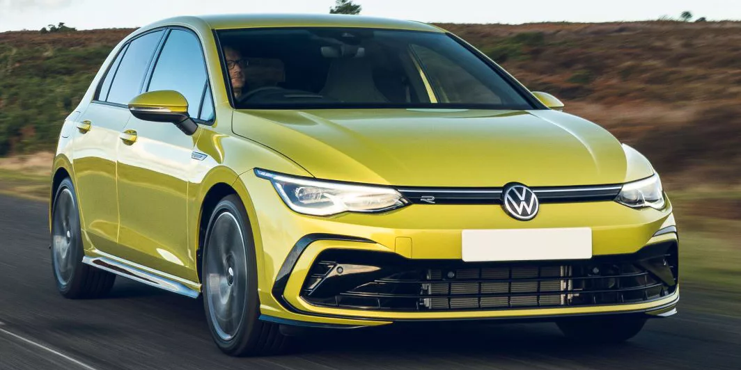 A yellow VW Golf driving on an open, rural road.