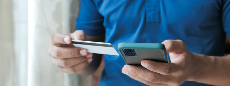 A person using their phone whilst holding a credit card, representing online payments.