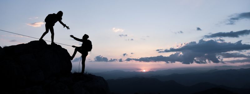 One person reaches out and helps someone below up onto a surface.