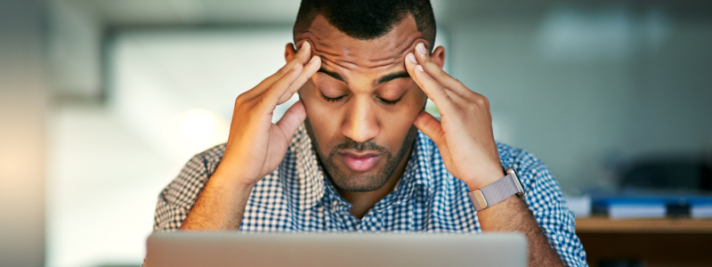 A person looking at their laptop with their hands resting on their forehead, appearing stressed.