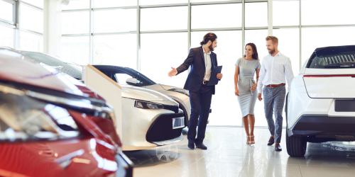 A couple are escorted round a showroom but someone in a suit, likely a car dealer.
