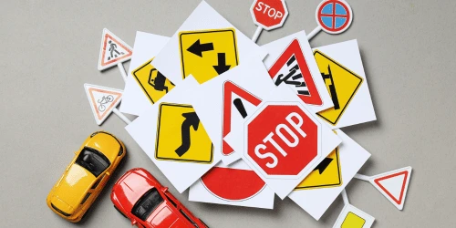 Print outs of road signs piled together, with toy cars at the side, symbolising a driving test.