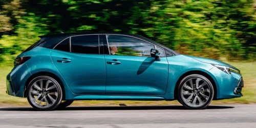 A teal Toyota Corolla Hybrid side on, driving in a rural setting.