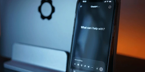 A phone showing ChatGPT, with the logo on a device in the background.