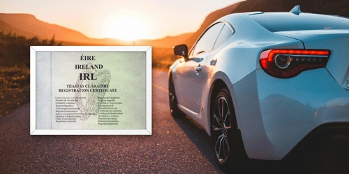 A white car on a road with a framed Irish vehicle log book in shot next to it.