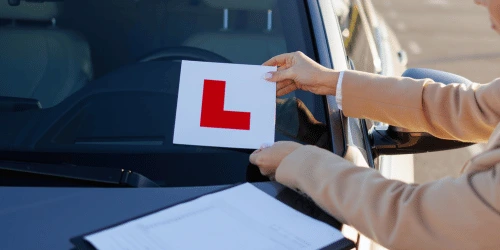 A learner sticker being placed onto a car windscreen.