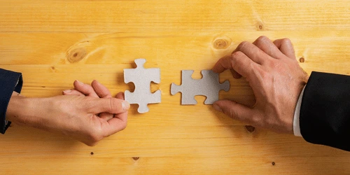 Two business people joining jigsaw pieces together.