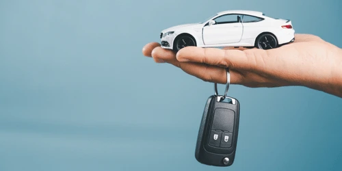 A hand with a model car and keys hanging down.